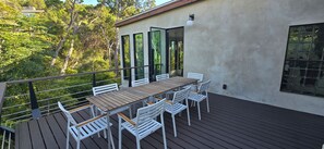 Eine Terrass mit Holztisch und weißen Stühlen, umgeben von Glastüren und Fenstern.