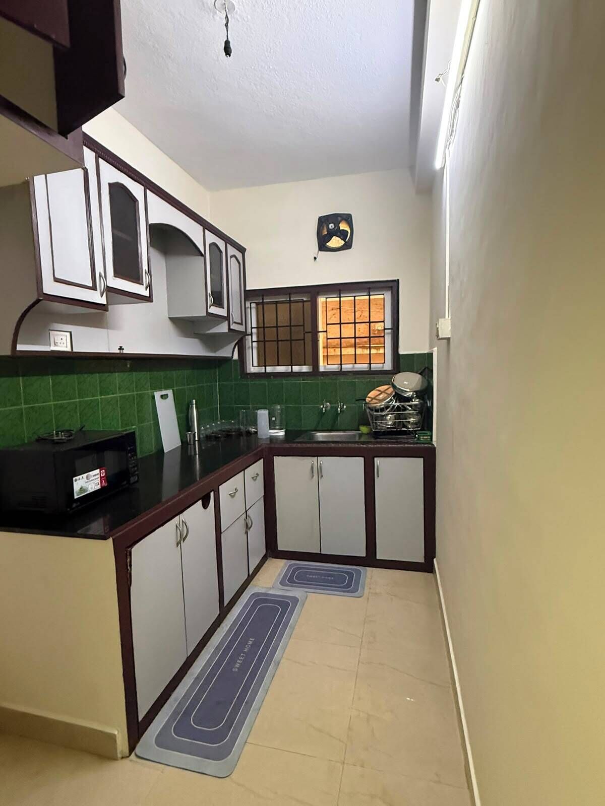 A compact kitchen with white cabinets, a microwave, and a window with bars.