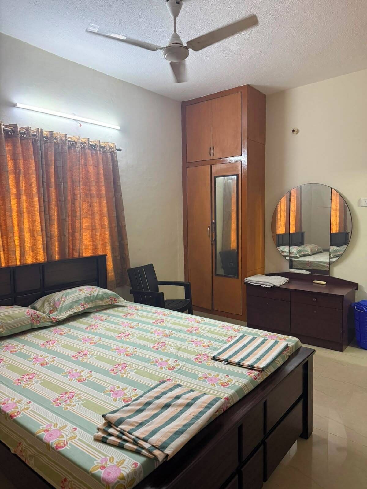 Un dormitorio con cama, armario, escritorio, silla, ventilador de techo y espejo.