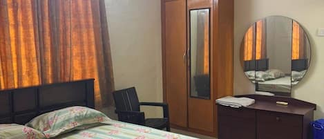 Un dormitorio con cama, armario, escritorio, silla, ventilador de techo y espejo.