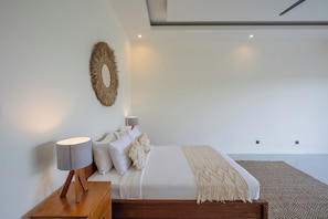 Ein Schlafzimmer mit einem Bett, Nachttischlampen, einem Wandspiegel und einem Teppich mit Struktur.