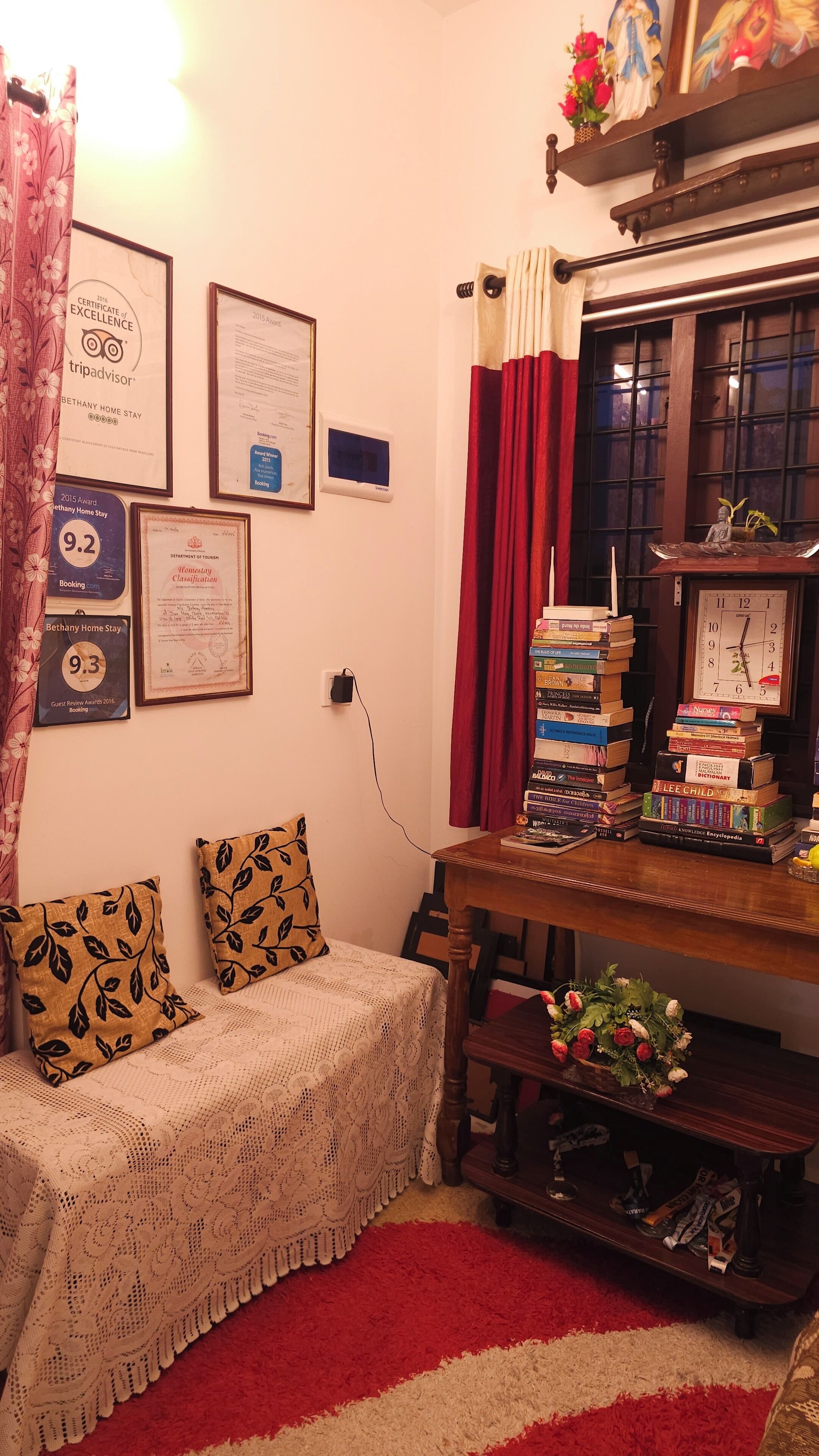 A cozy room with a sofa, a stack of books, certificates on the wall, and a clock.