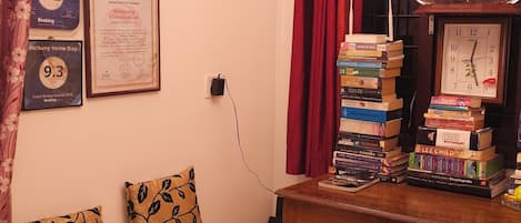 Una habitación acogedora con un sofá, libros apilados, diplomas en la pared y un reloj.