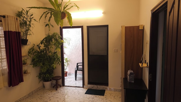 A room with a tiled floor, a potted plant, a chair, and a door leading to another space.