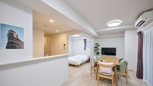 Una habitación de hotel moderna con una cama, un área de comedor con una mesa y sillas, un televisor y un equipo de aire acondicionado.