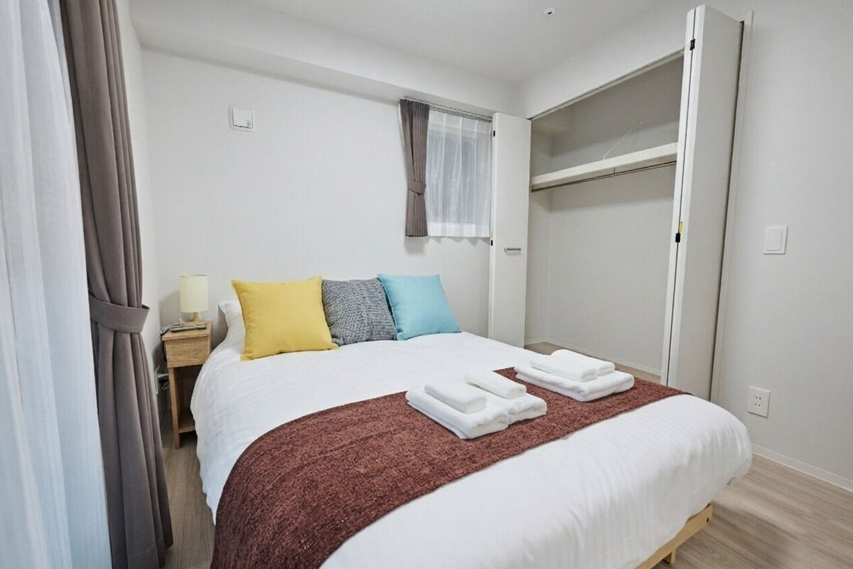 Ein Hotelzimmer mit Bett, Nachttisch, Lampe, Kleiderschrank und einem Fenster mit Vorhängen.