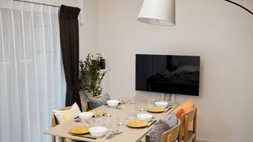 A dining area with a table set for two, a television mounted on the wall, and a plant on the table.