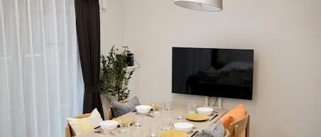 Un comedor con una mesa dispuesta para dos personas, un televisor montado en la pared y una planta sobre la mesa.