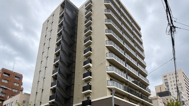 Un edificio residencial de varios pisos con balcones, fachada plana y un estacionamiento al frente.