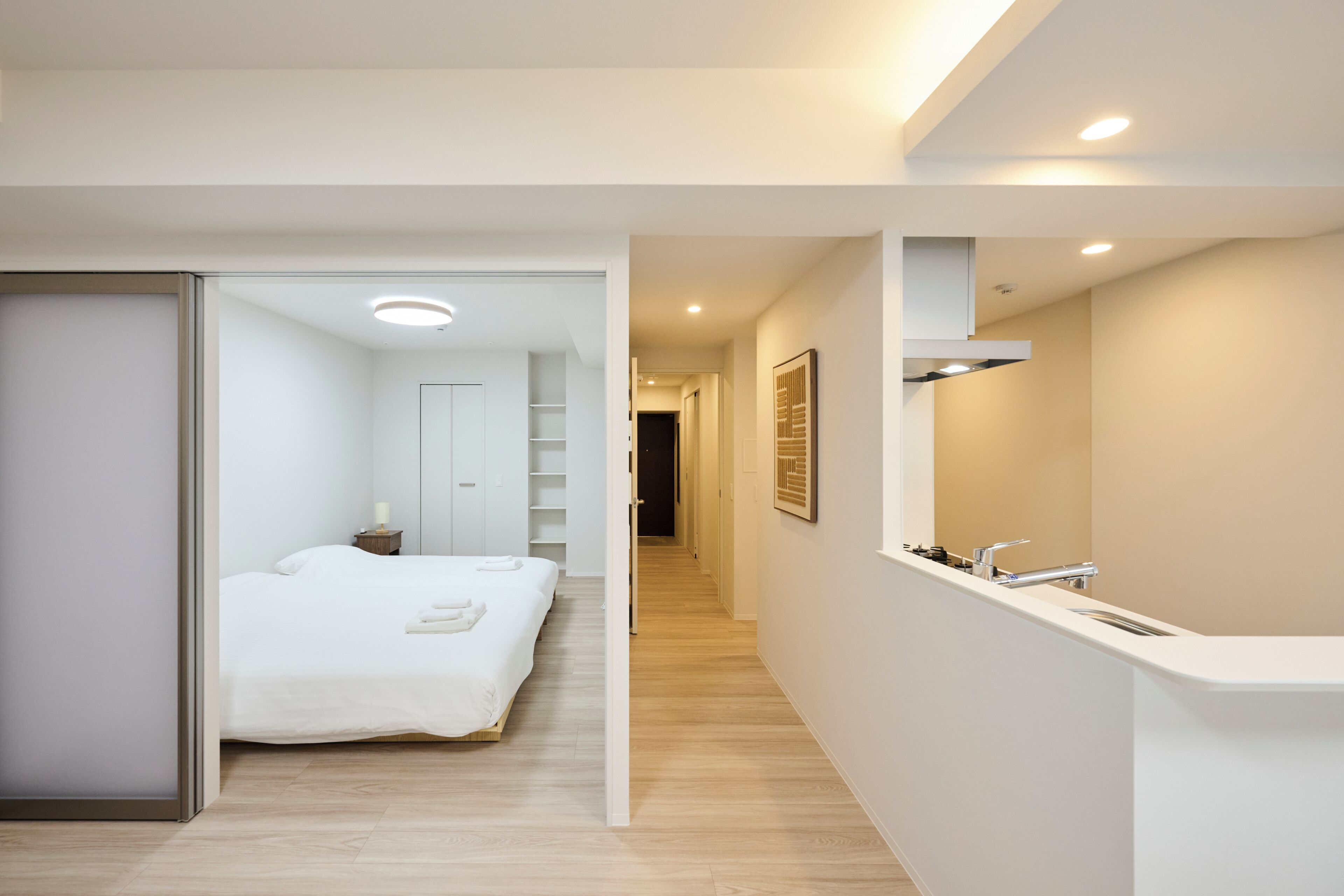 A modern hotel room with a bed, bedside table, and a bathroom with a sink and mirror.