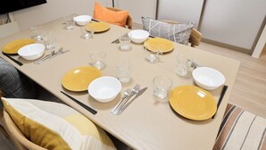 Una mesa de comedor preparada con platos amarillos y blancos, vasos transparentes y cubiertos.