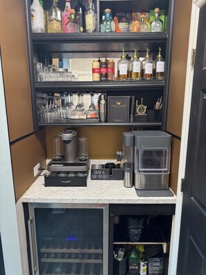 A bar area with shelves of liquor bottles, glasses, and a coffee machine.