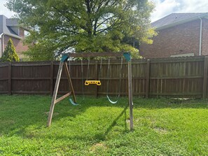 A wooden swing set in a backyard with a wooden fence and a tree in the background.