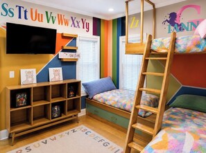 A child's bedroom with bunk beds, a TV, a bookshelf, and a colorful alphabet wall.
