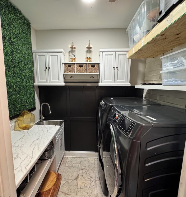 A compact kitchen with a washing machine, white cabinets, and a green wall.
