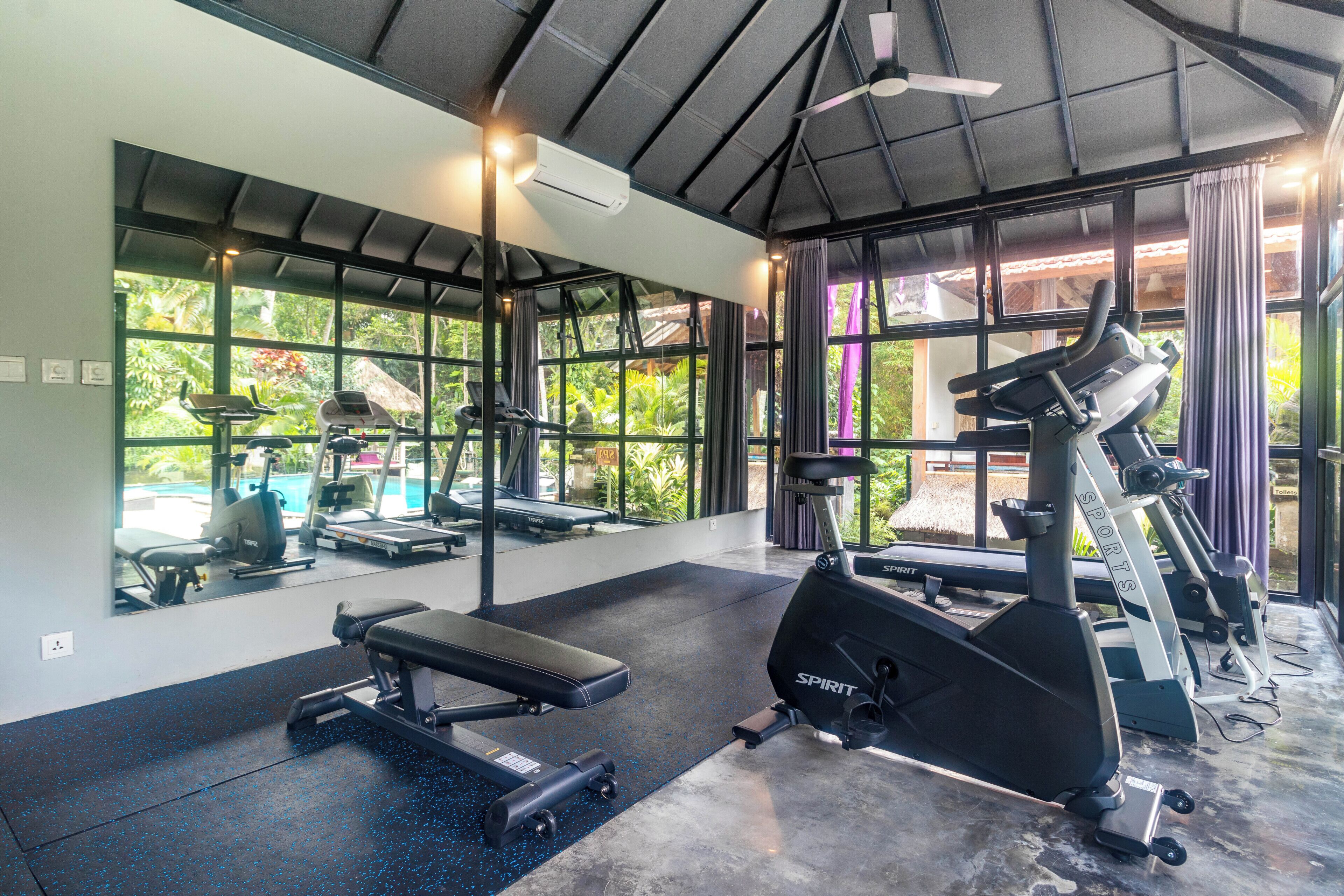 Une salle de sport équipée de matériel d’exercice, dotée de grandes fenêtres et d’un ventilateur de plafond.