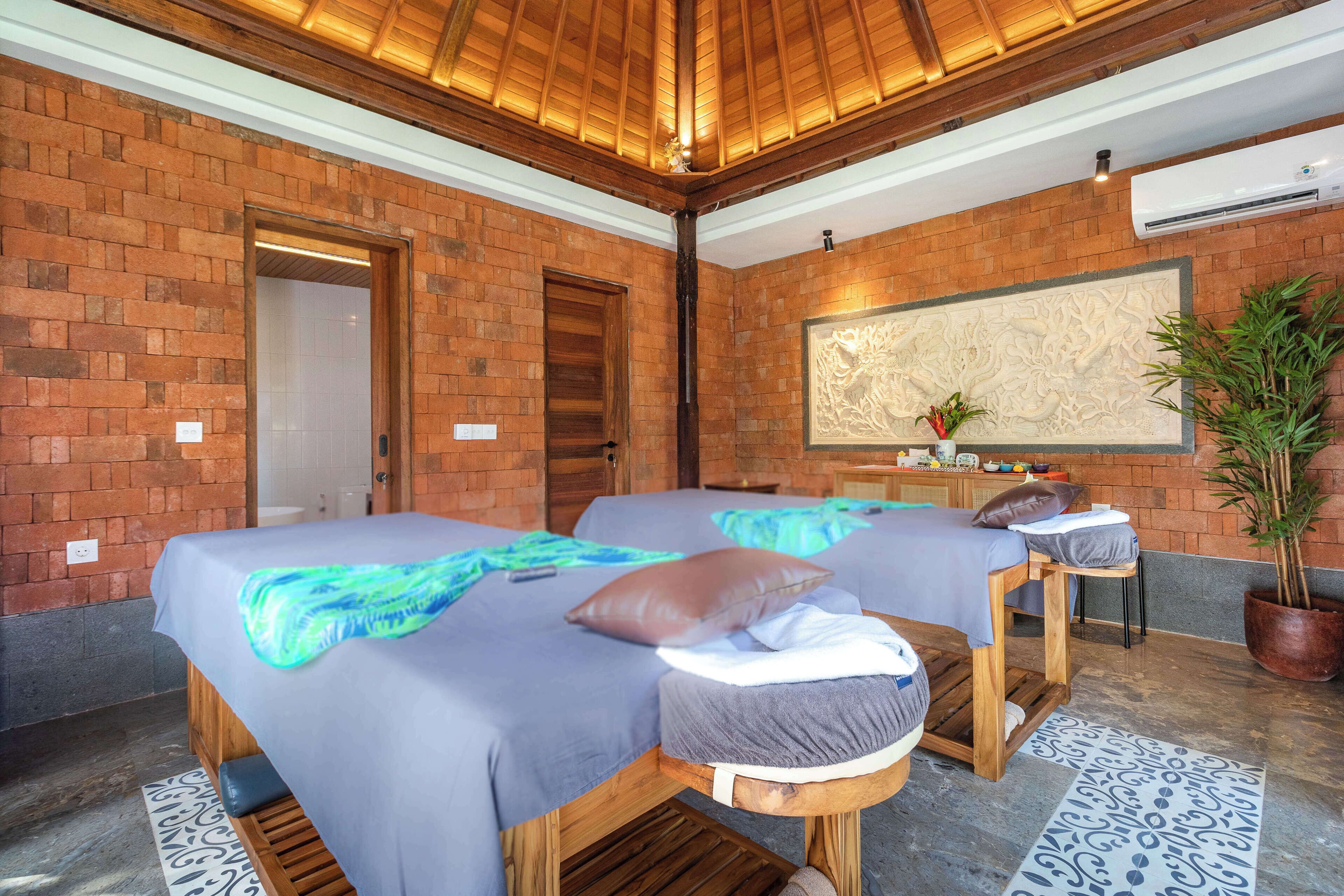 Una habitación con dos camas, techo de madera, pared de ladrillo y un panel decorativo grande.