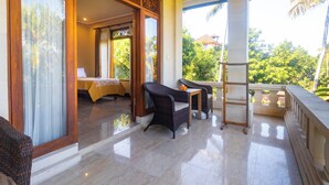 A room with a bed, a table with chairs, and a balcony with a view of greenery and buildings.
