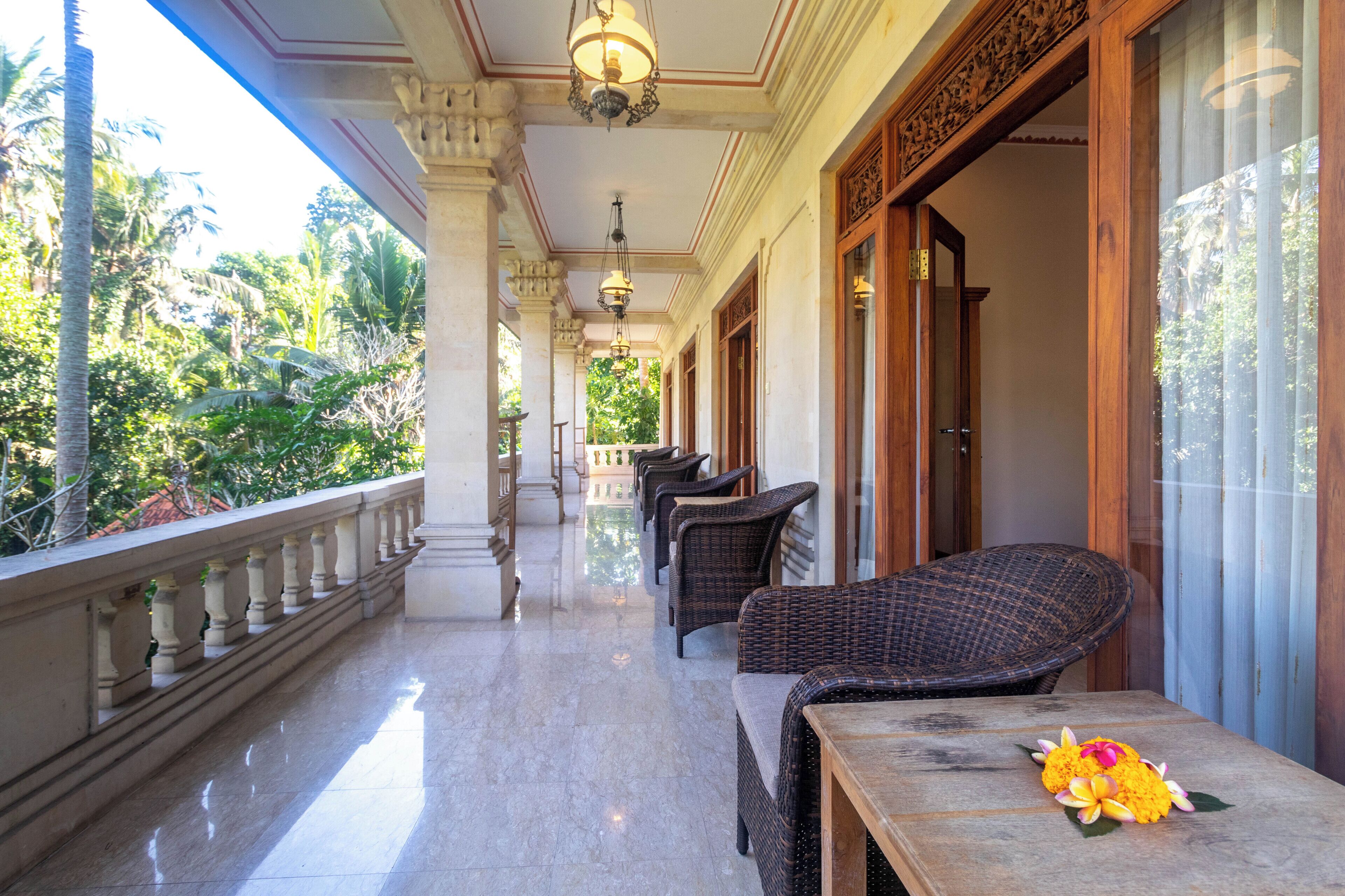 A balcony with wicker furniture and a flower arrangement, overlooking a garden.