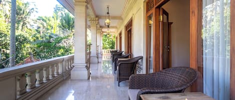 A balcony with wicker furniture and a flower arrangement, overlooking a garden.