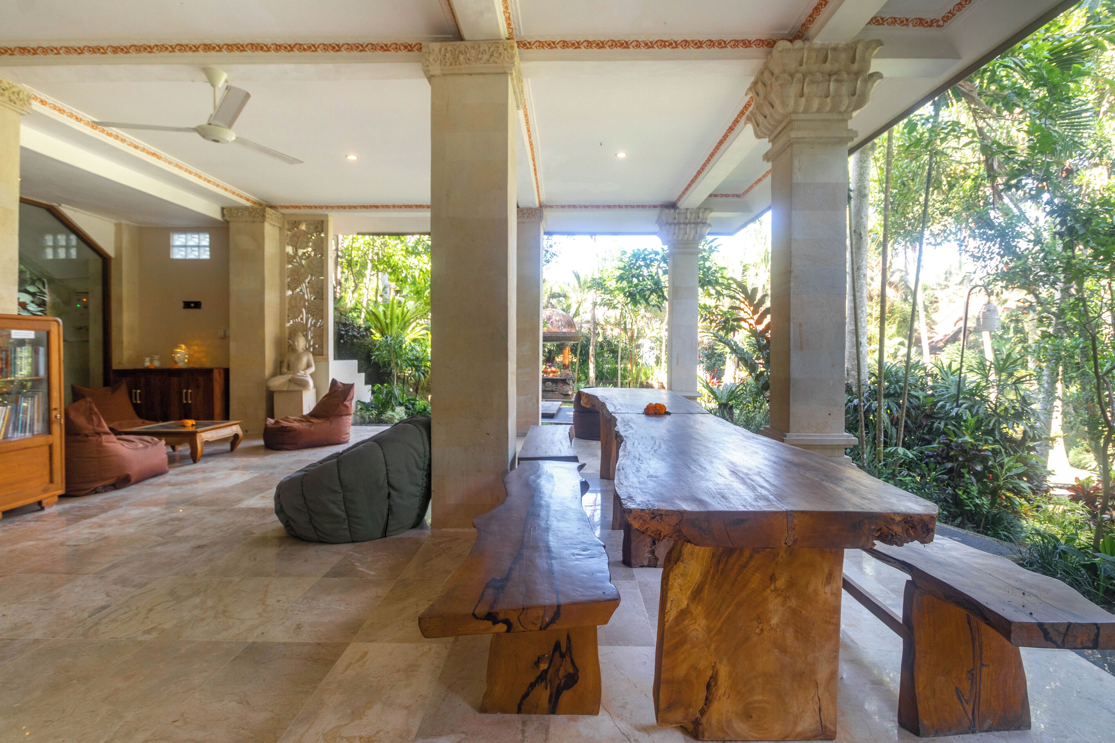 Un espacio interior amplio con una larga mesa de madera, asientos cómodos y vistas a abundante follaje en el exterior.