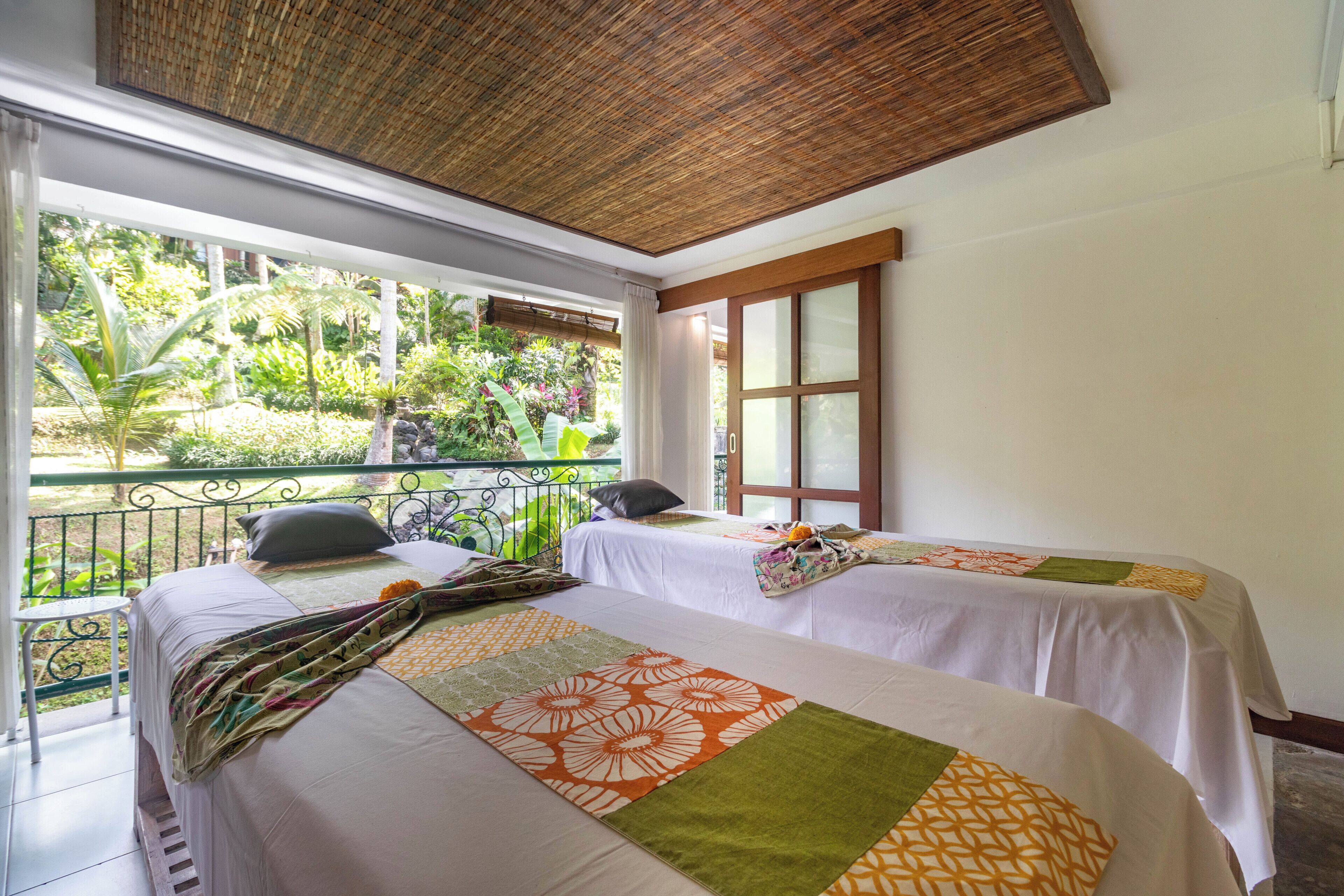 A room with two beds, a balcony, and a view of greenery.