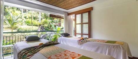 A room with two beds, a balcony, and a view of greenery.