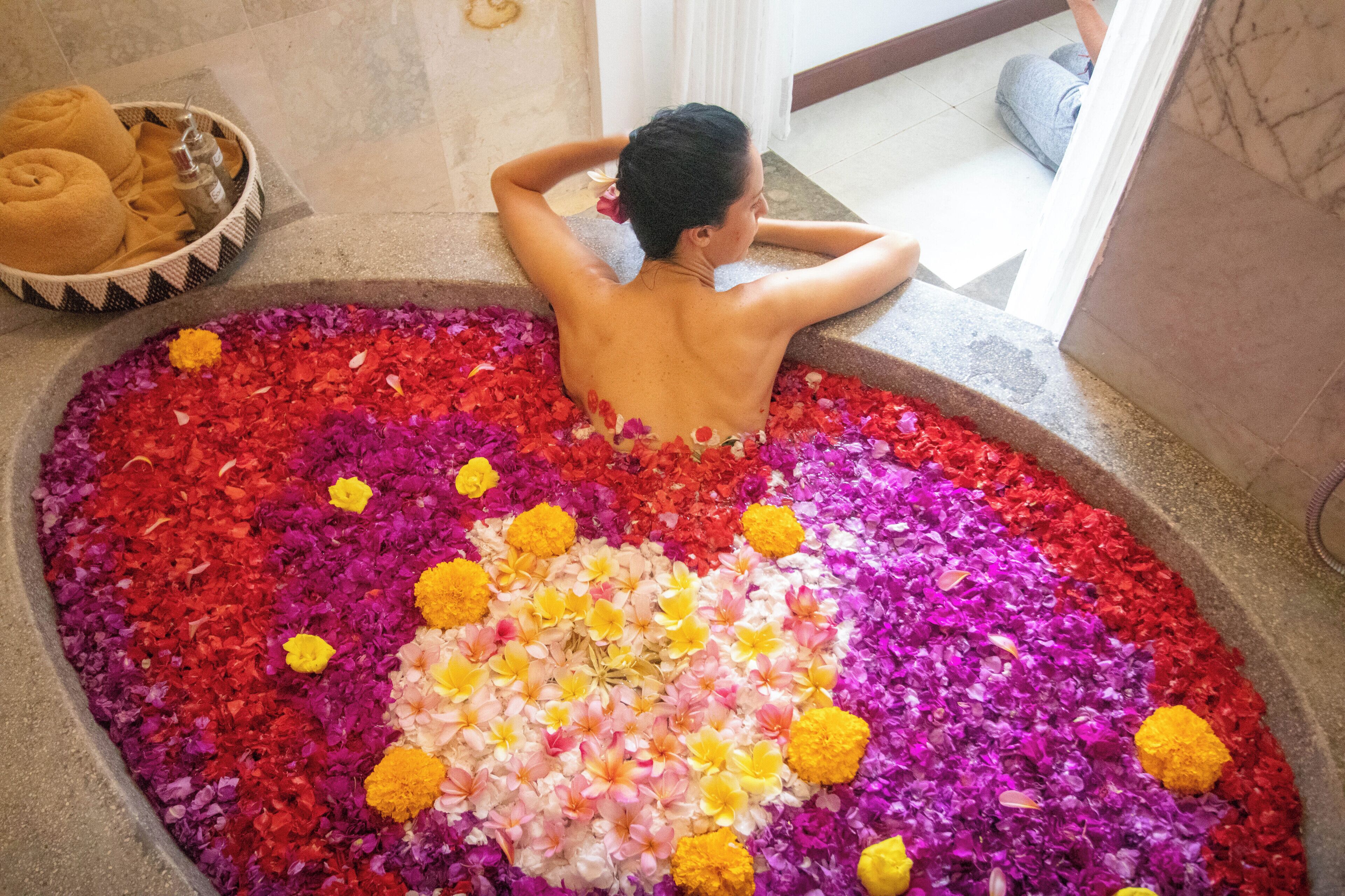 Une personne se détend dans une baignoire remplie de pétales de fleurs.