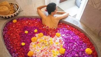 Una persona relajándose en una bañera llena de pétalos de flores.