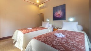 A hotel room with two single beds, each with a red patterned bedspread and white pillows. There is a painting of a flower on the wall, and a telephone on the nightstand.