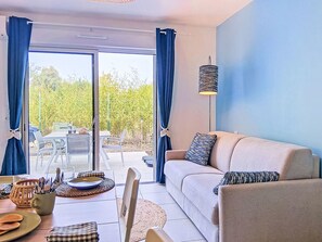 A modern living room with a sofa, dining table, and a view of a garden through large glass doors. - Les Bains d'Oléron 2 by Interhome (Ile d'Oléron)