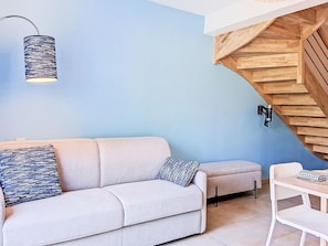 A modern living room with a light-colored sofa, patterned cushions, a wooden staircase, and a hanging light fixture. - Les Bains d'Oléron 2 by Interhome (Ile d'Oléron)