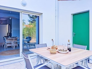 Uma área de refeições ao ar livre com uma mesa, cadeiras e uma garrafa de vinho.