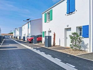 Uma rua com edifícios brancos, persianas verdes e carros estacionados.