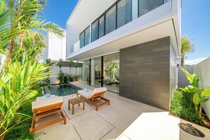 A modern outdoor pool area with lounge chairs and a table, surrounded by tropical plants. - Nusa Dua Ocean View Luxury Villas (Kuta Selatan)