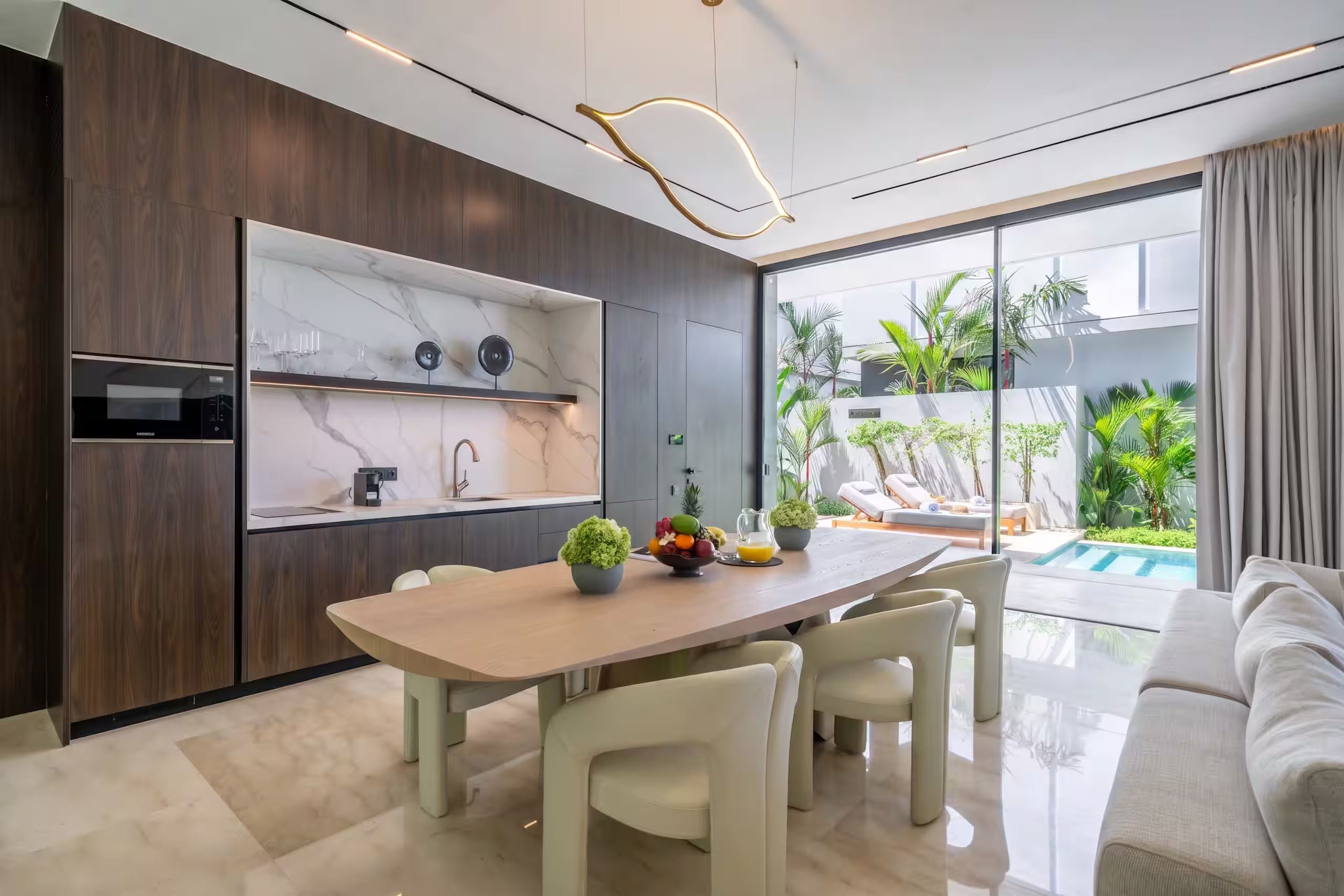 Cocina moderna con salpicadero de mármol, comedor con mesa y sillas, y vistas a una piscina y jardines.