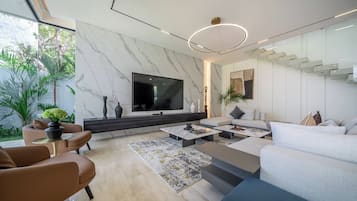 A modern living room with a flat-screen TV, a sofa, a coffee table, and a dining area.