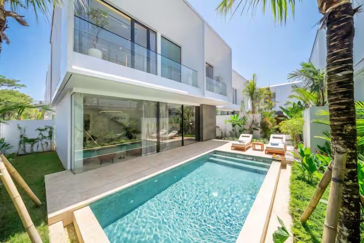 A modern house with a swimming pool, glass doors, and a patio with lounge chairs.