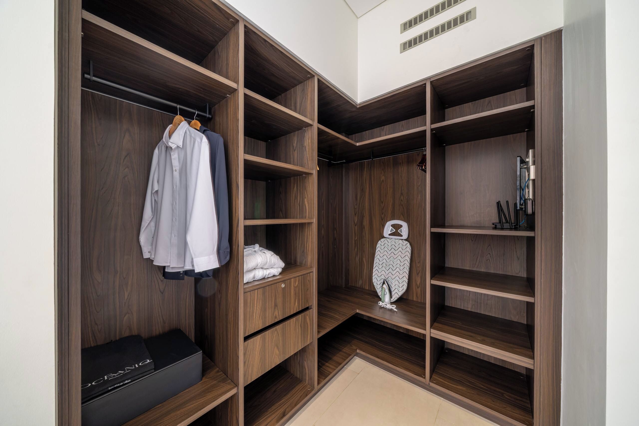 Un vestidor amplio con varios estantes y espacio para colgar ropa, un zapatero y una plancha pequeña.