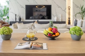 Un salon moderne avec une cheminée en marbre, une table basse sur laquelle se trouve un panier de fruits et une carafe de jus d’orange, ainsi qu’un magazine posé sur la table.