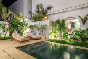 A modern outdoor pool area with lounge chairs and tropical plants.