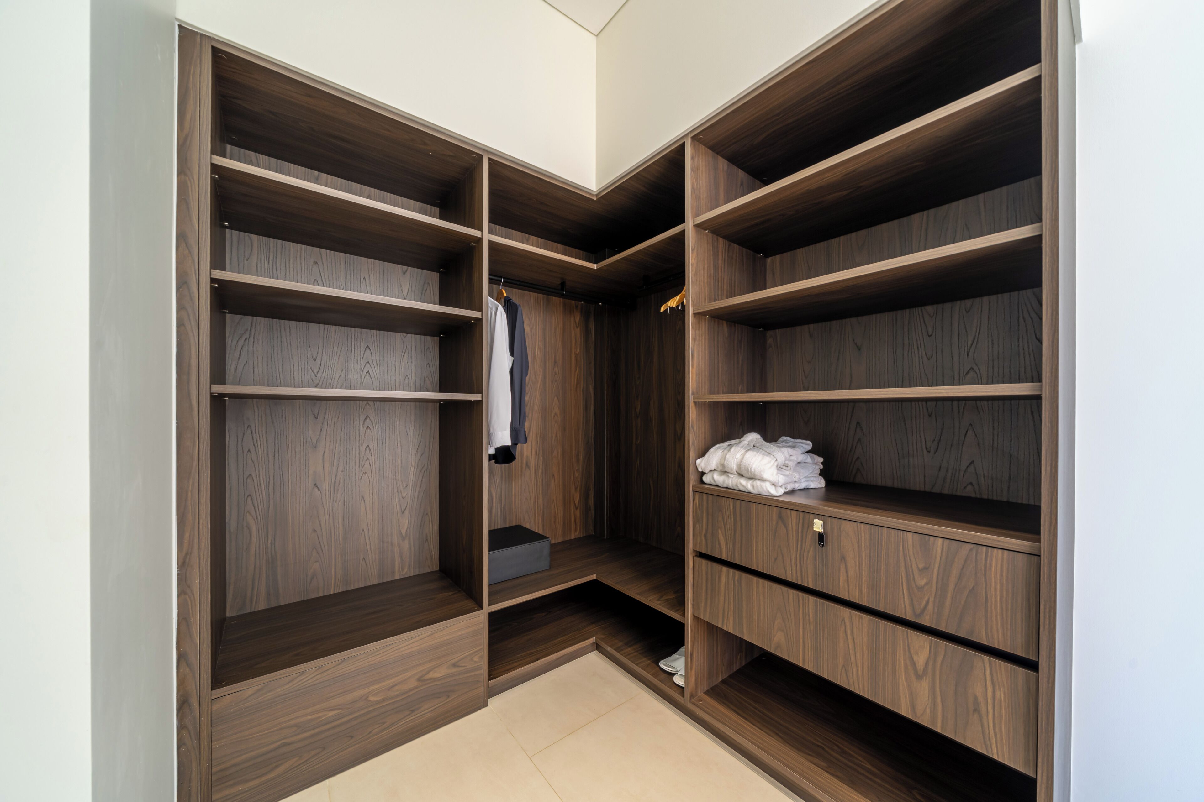 Un vestidor amplio con varios estantes de madera y una barra para colgar, con una paleta de colores neutros y piso de baldosas.