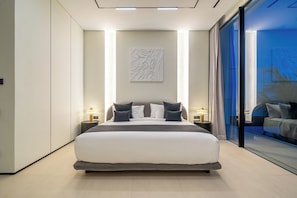 Une chambre moderne avec un grand lit, des lampes de chevet, une œuvre d’art accrochée au mur et une vue à travers une porte vitrée.