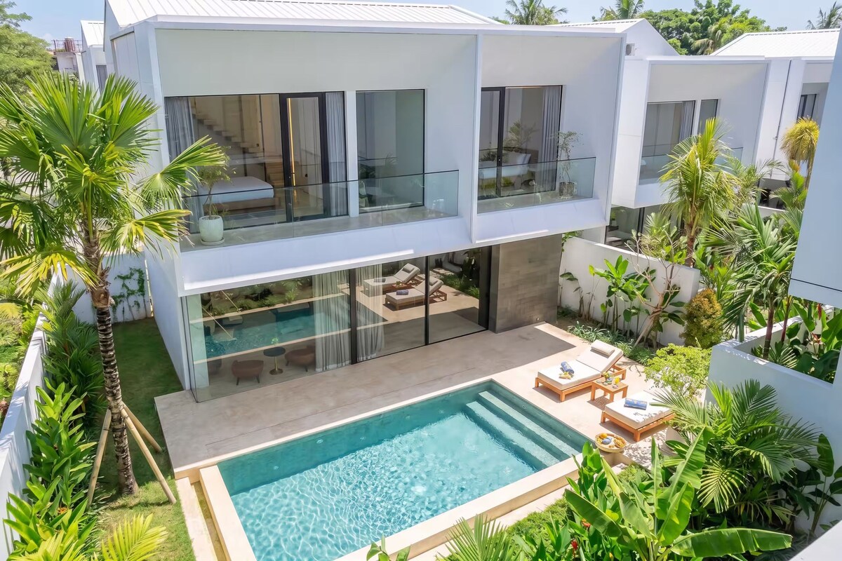 A modern two-story house with a swimming pool, outdoor seating, and lush greenery.