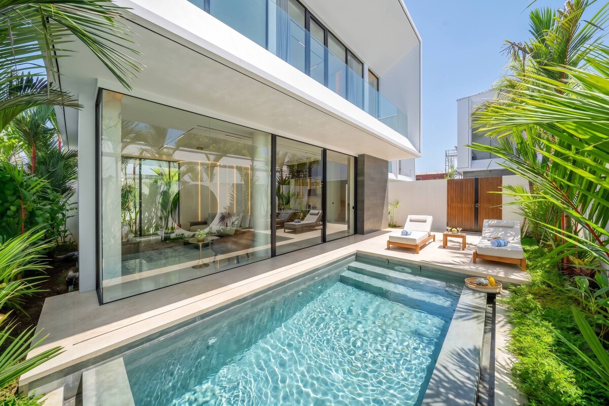 A modern house with a glass-enclosed patio, a swimming pool, and outdoor furniture.