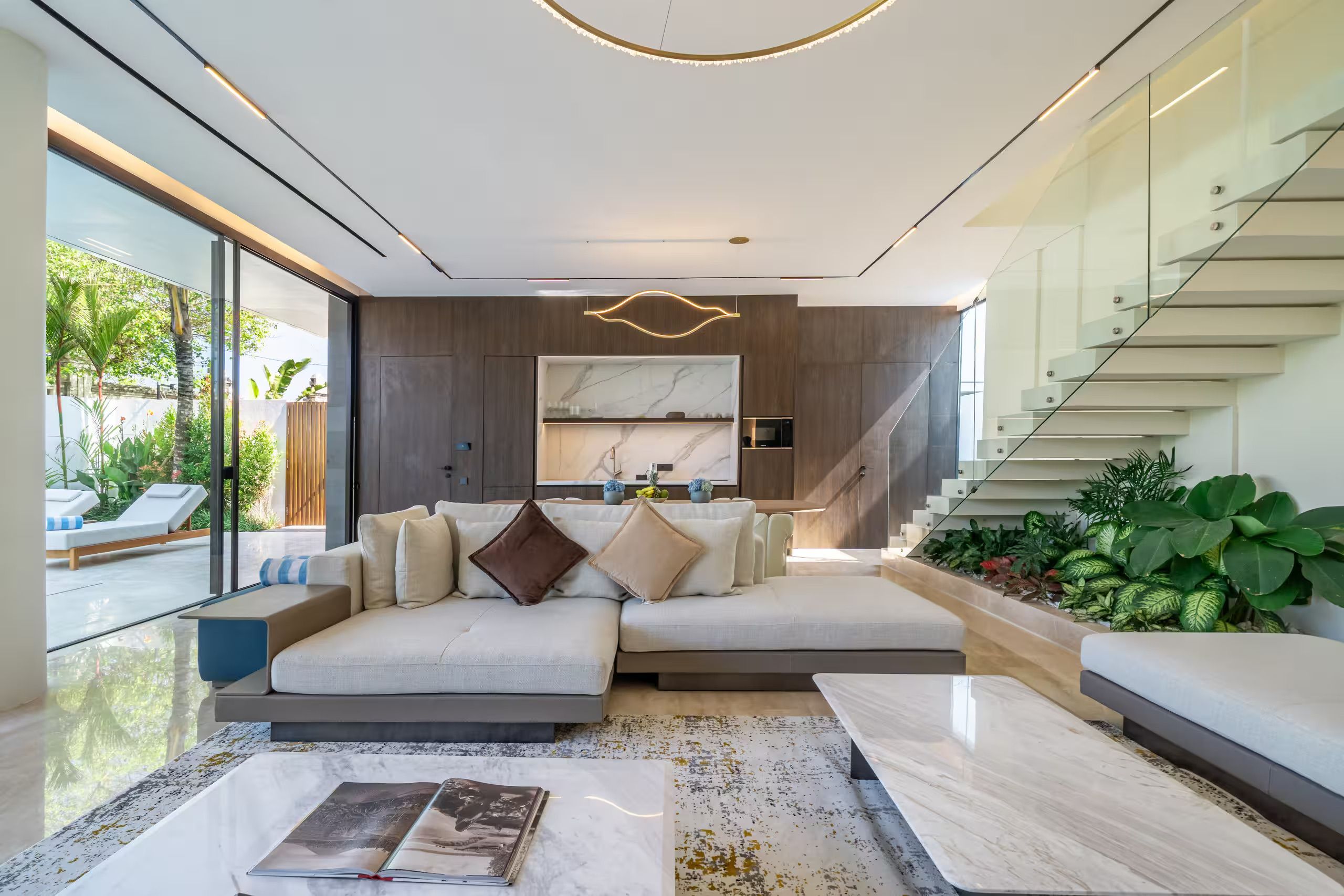 A modern living room with a sectional sofa, a marble coffee table, and a staircase with glass railings.