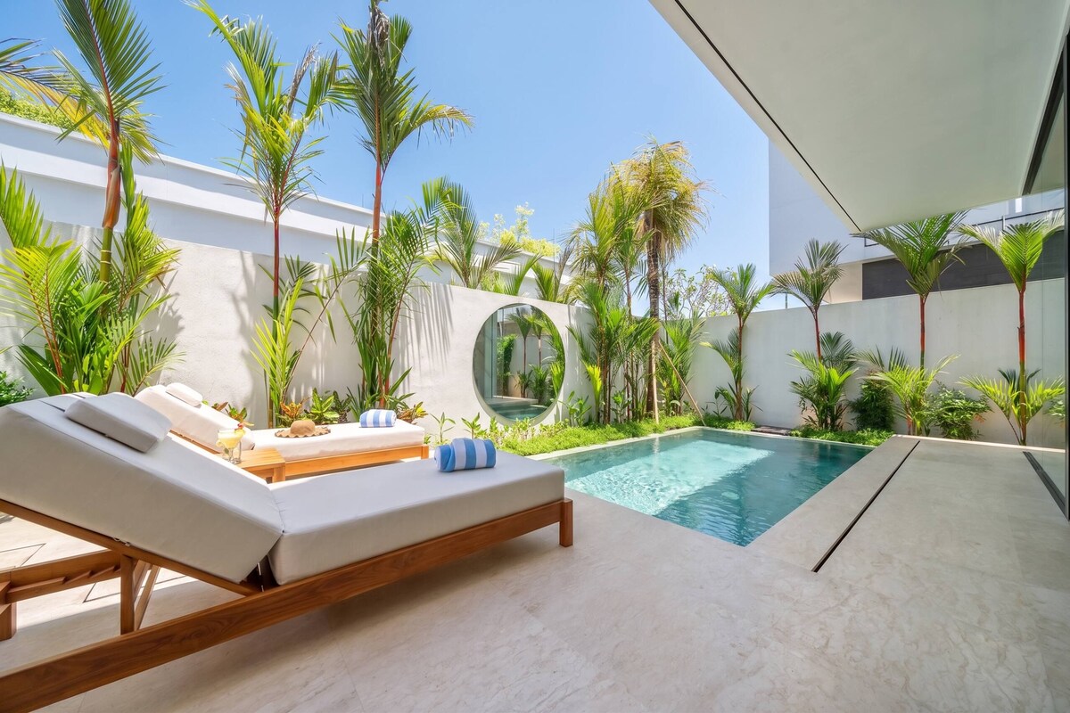 A modern outdoor pool area with lounge chairs and tropical plants.