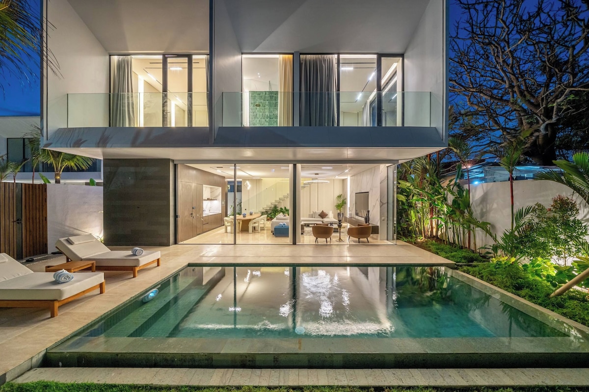 A modern two-story house with a swimming pool, glass doors leading to a dining area, and a view of the surrounding landscape.