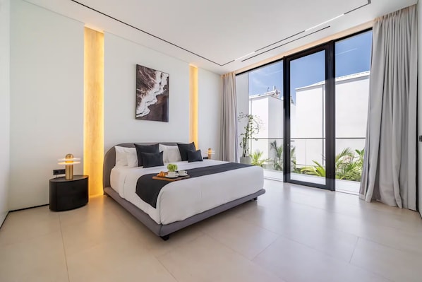 Un dormitorio moderno con una cama grande, una mesita de noche, una obra de arte colgada en la pared y vistas a través de un ventanal corredero.