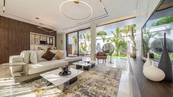 A modern living room with a sofa, coffee table, and a view of a pool and greenery outside.